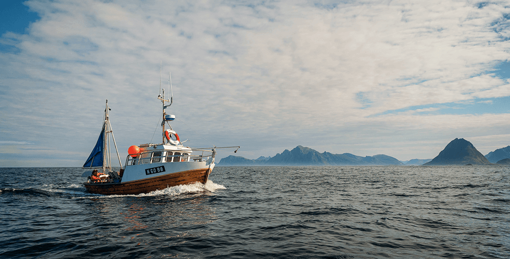 Kleine Noorse vissersboot op zee met bergen aan de horizon